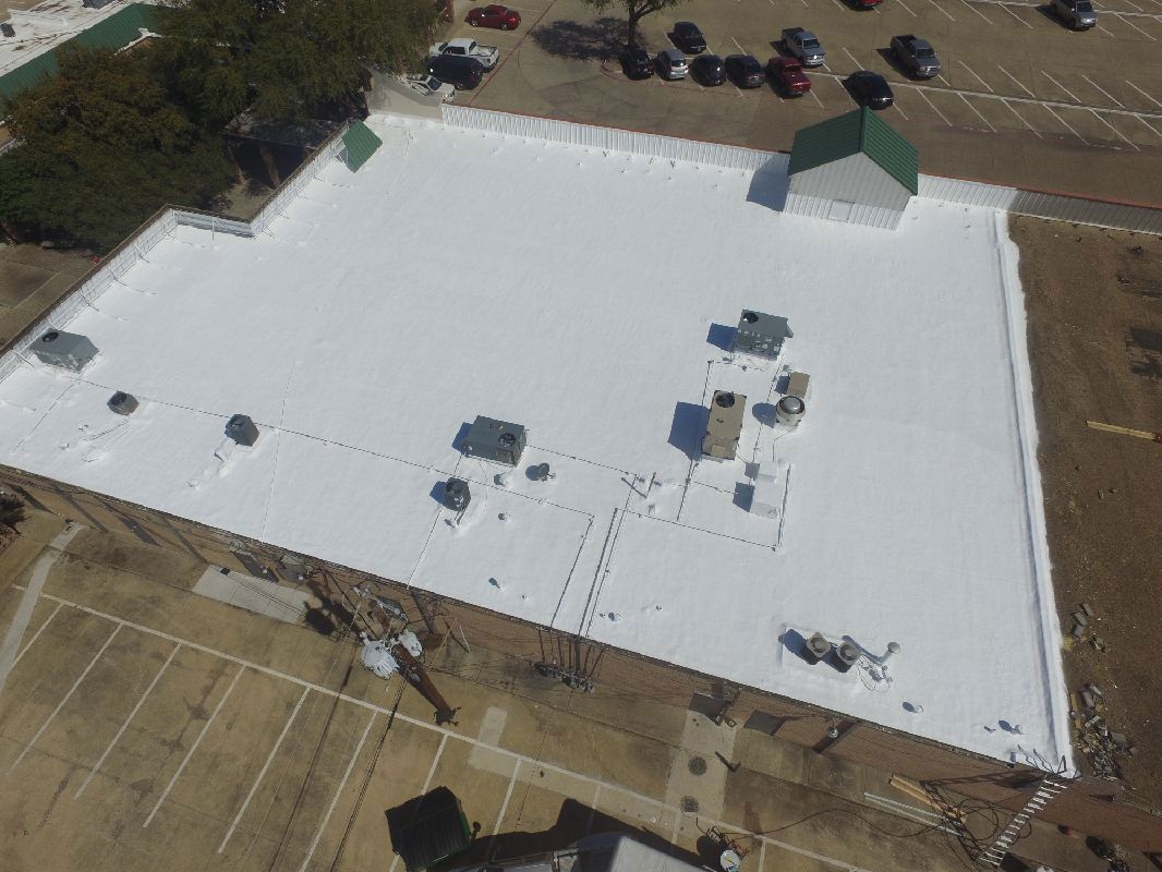 Overhead view of a flat, white commercial roof with various ventilation units and a small green-roofed structure.