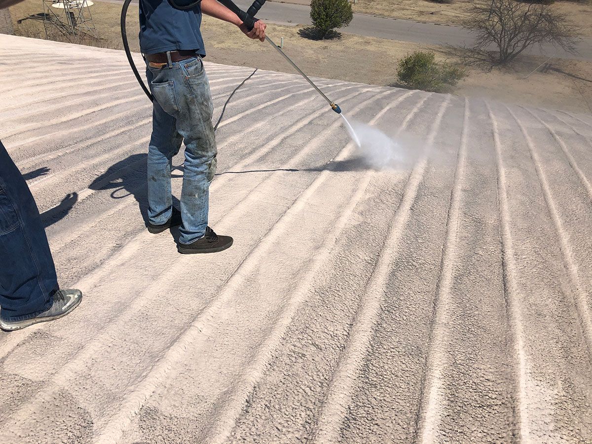 Man pressure washing a light-colored roof, spraying water in parallel lines.