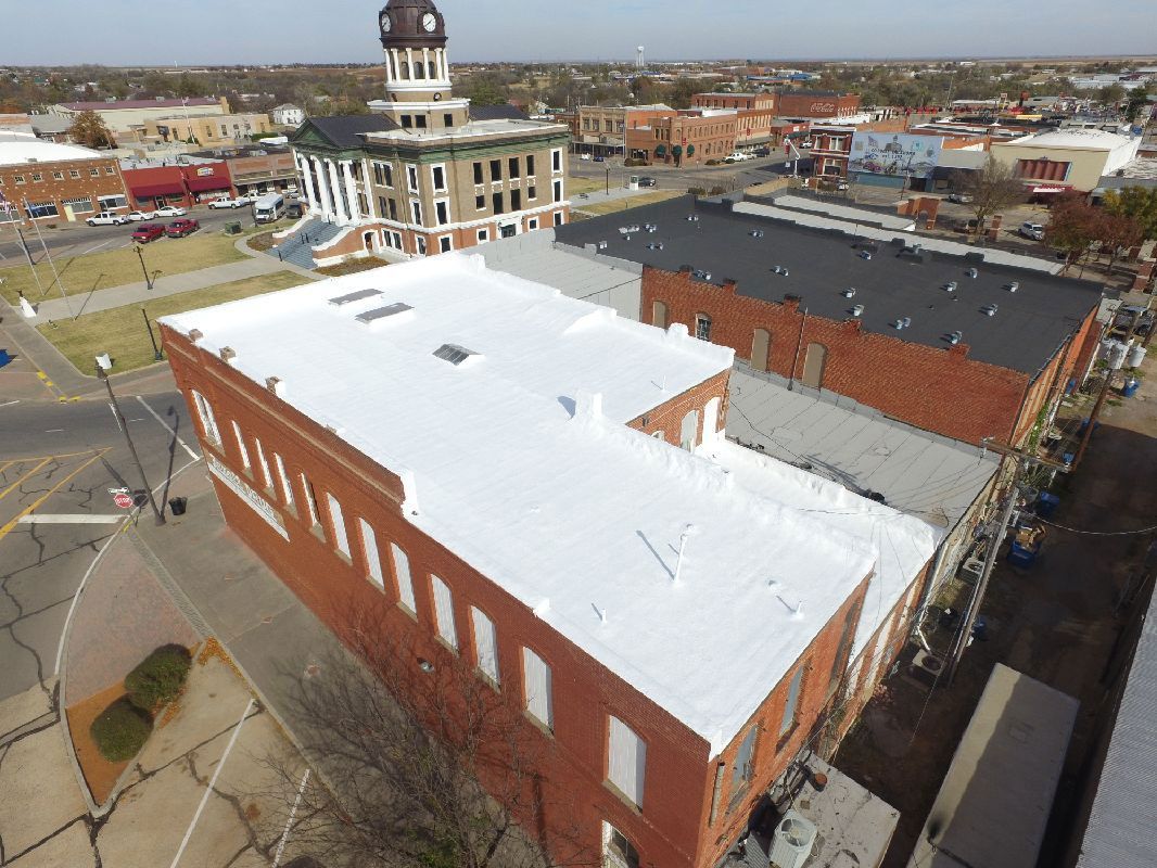 Aerial view of red brick buildings with white roofs in a small town; courthouse in the background.