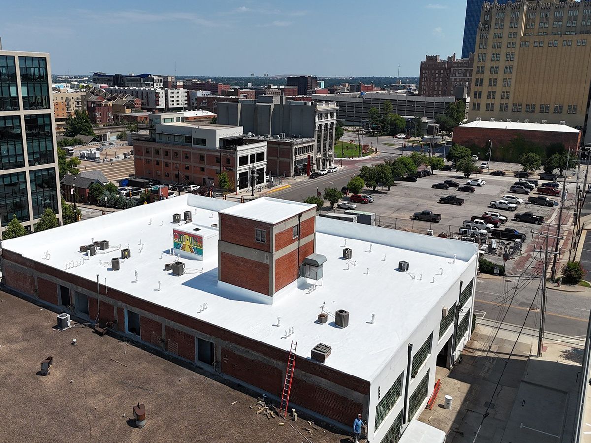 Aerial view of a brick building with a white roof in a city; cars and buildings in the background.