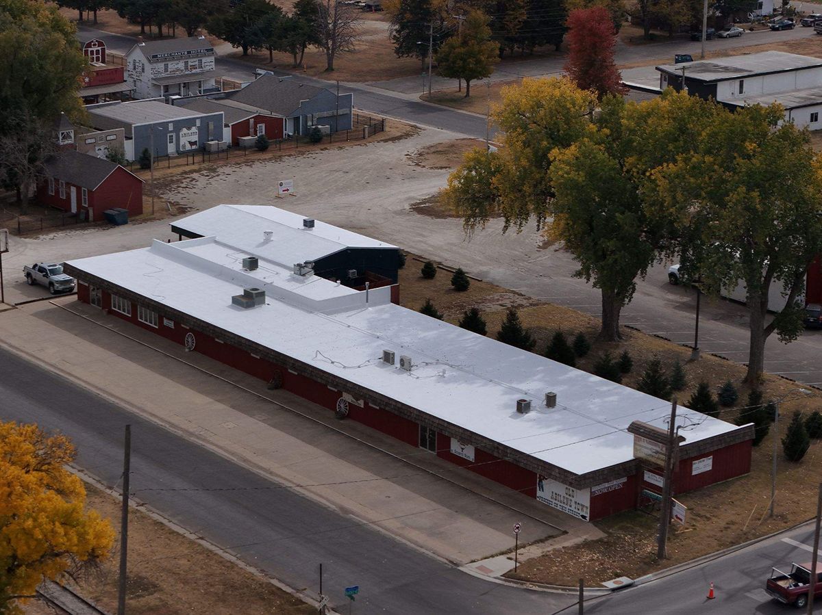 Aerial view of a long, single-story building with a red exterior, silver roof, and several air conditioning units.