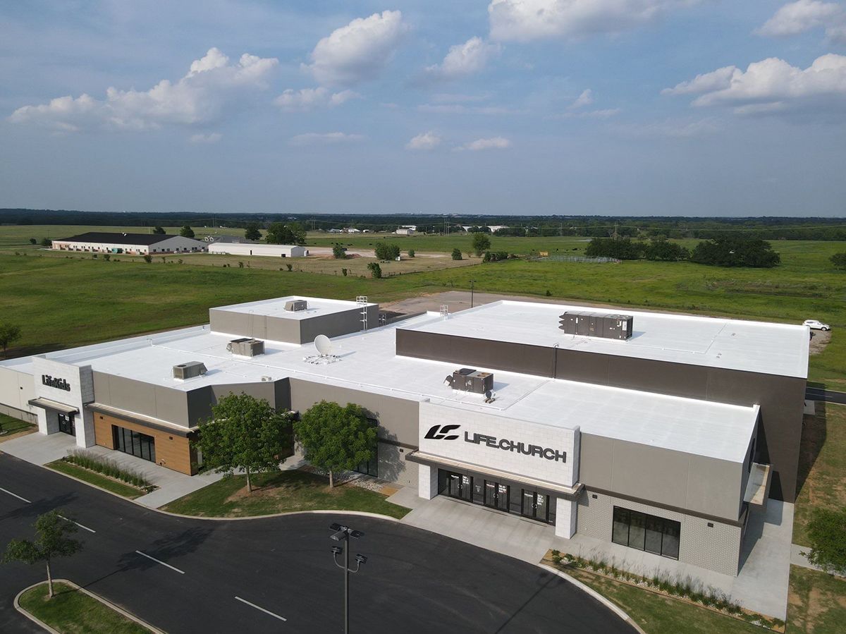 An aerial view of Life Church, a modern building with a flat roof, in a field under a blue sky.