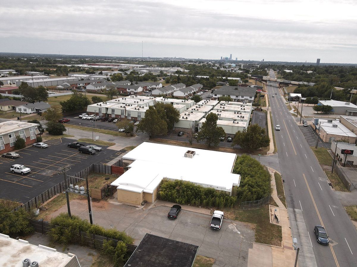 Aerial view of suburban area with buildings, roads, and trees. White-roofed building in the center.