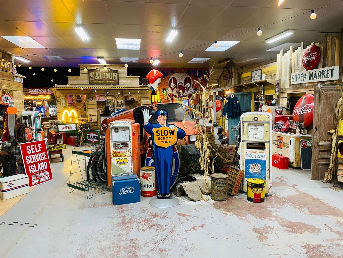 Intérieur d'une boutique vintage avec de vieilles pompes à essence, des panneaux et une silhouette tenant un panneau « RALENTIR ».
