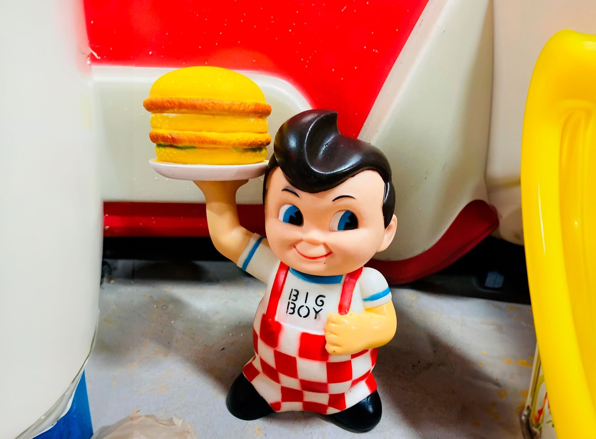Statue de Big Boy tenant un hamburger sur une assiette, tablier à carreaux rouges et blancs.