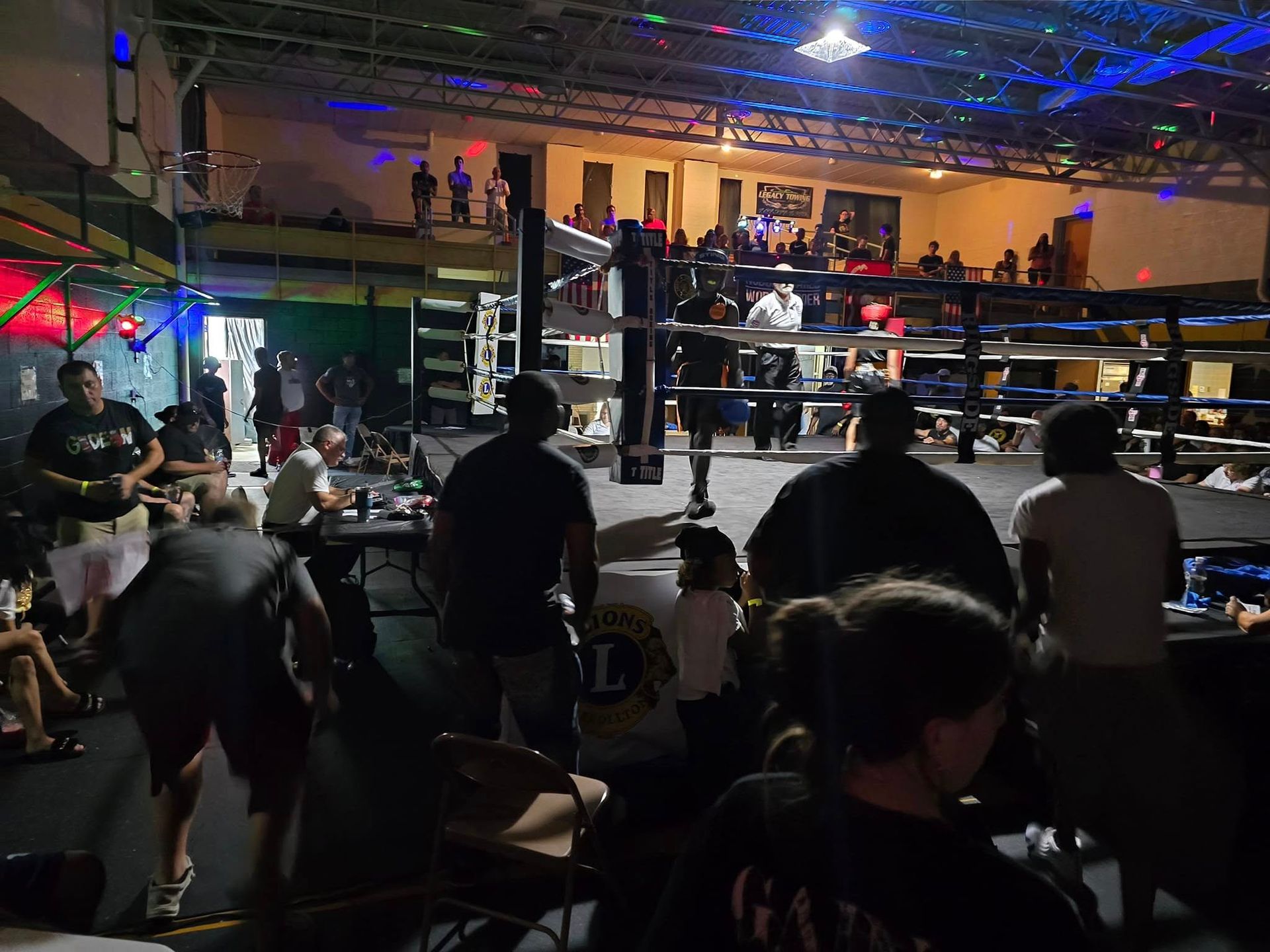 A group of people are watching a boxing match in a gym.