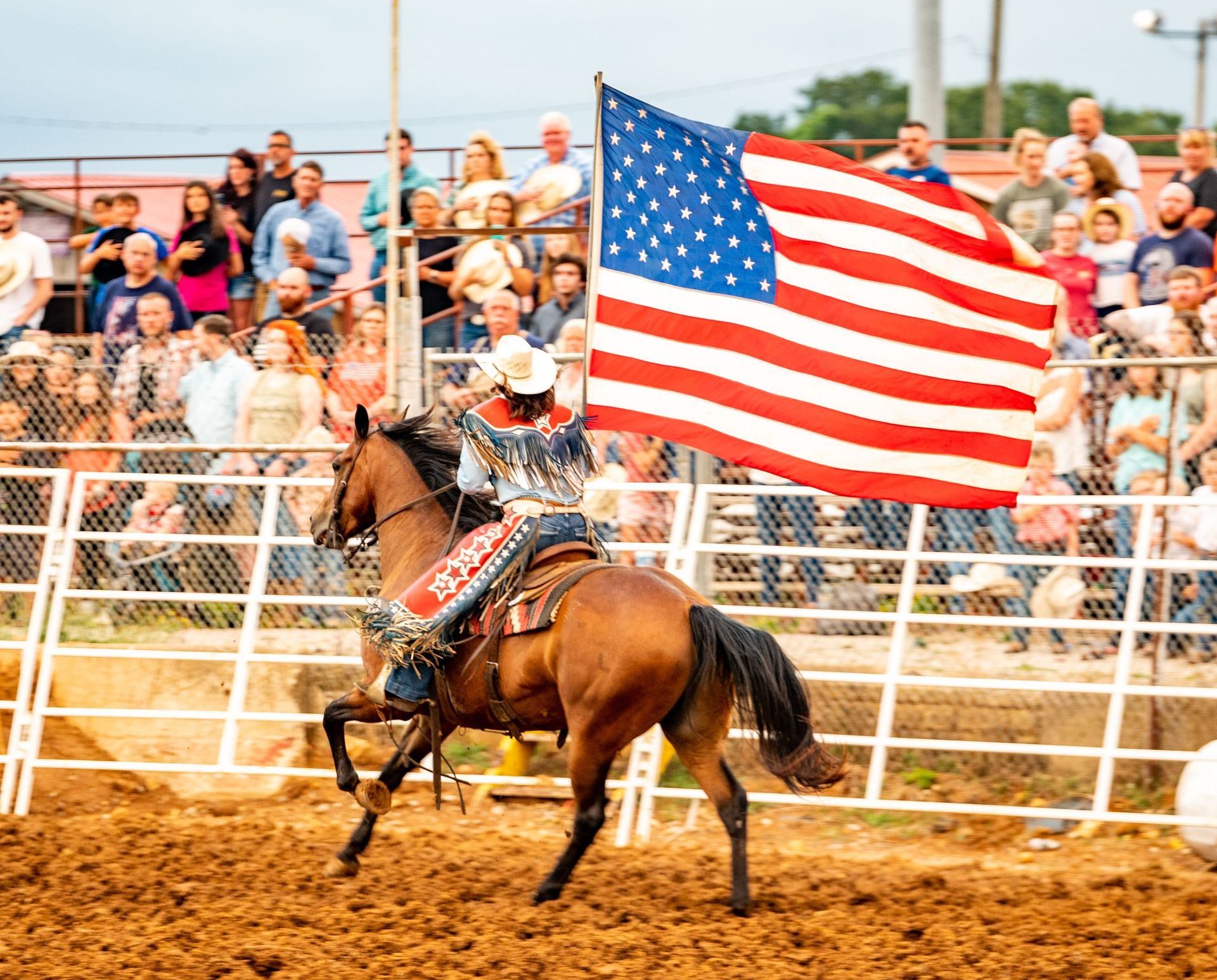 A man is riding a horse in a rodeo with an american flag in the background.