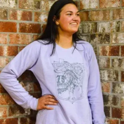 A woman wearing a purple sweatshirt is standing in front of a brick wall.