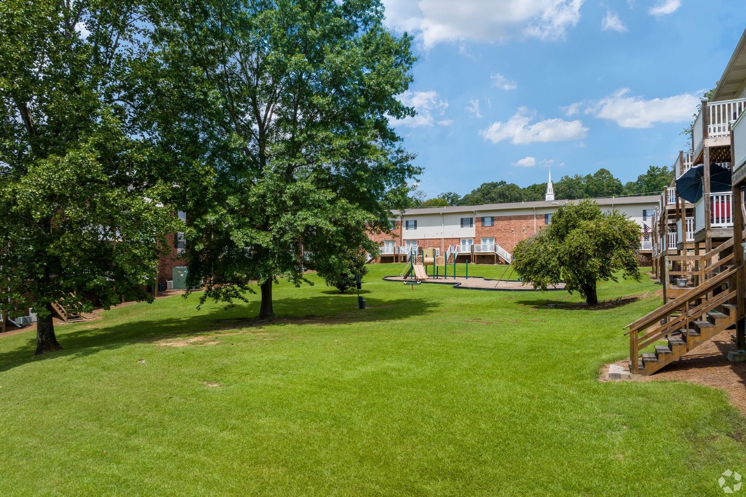 A large lush green field with trees in front of a building.
