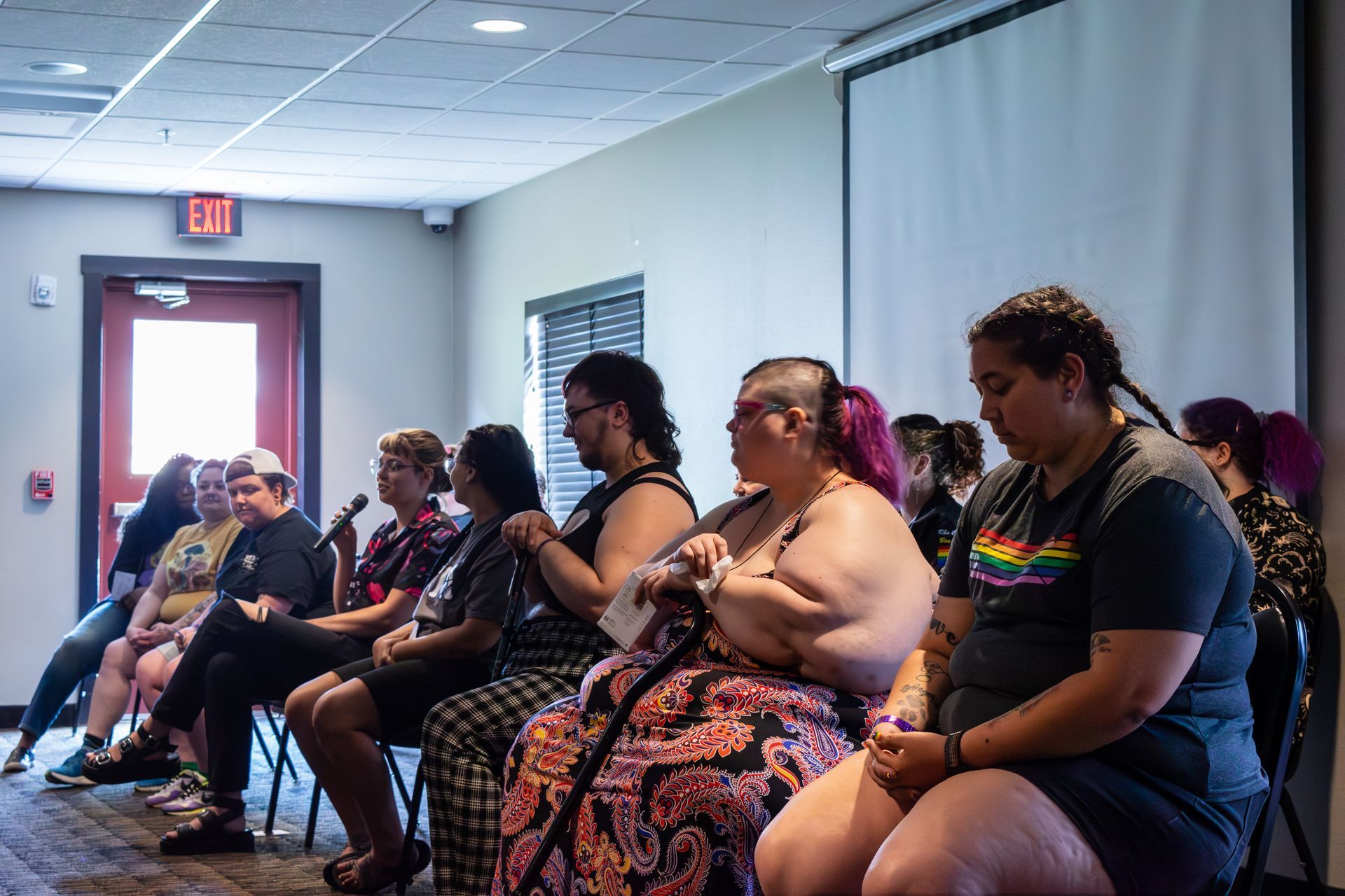 10 people seated in 2 rows of chairs, listening to one person speak on the microphone