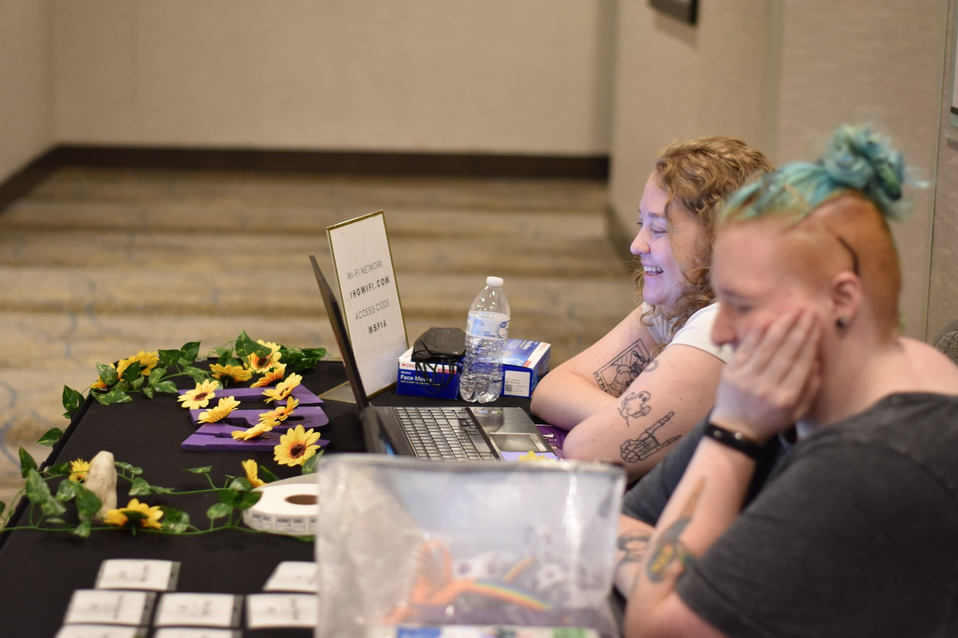 Two smiling people seated at a table with an array of GRL themed decorations and a laptop. 