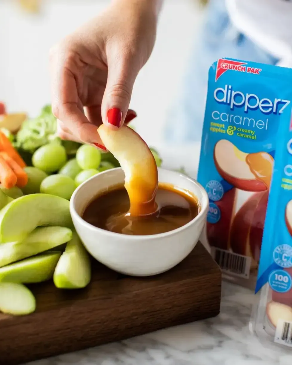 A person is dipping a DIPPERZ apple into a bowl of caramel