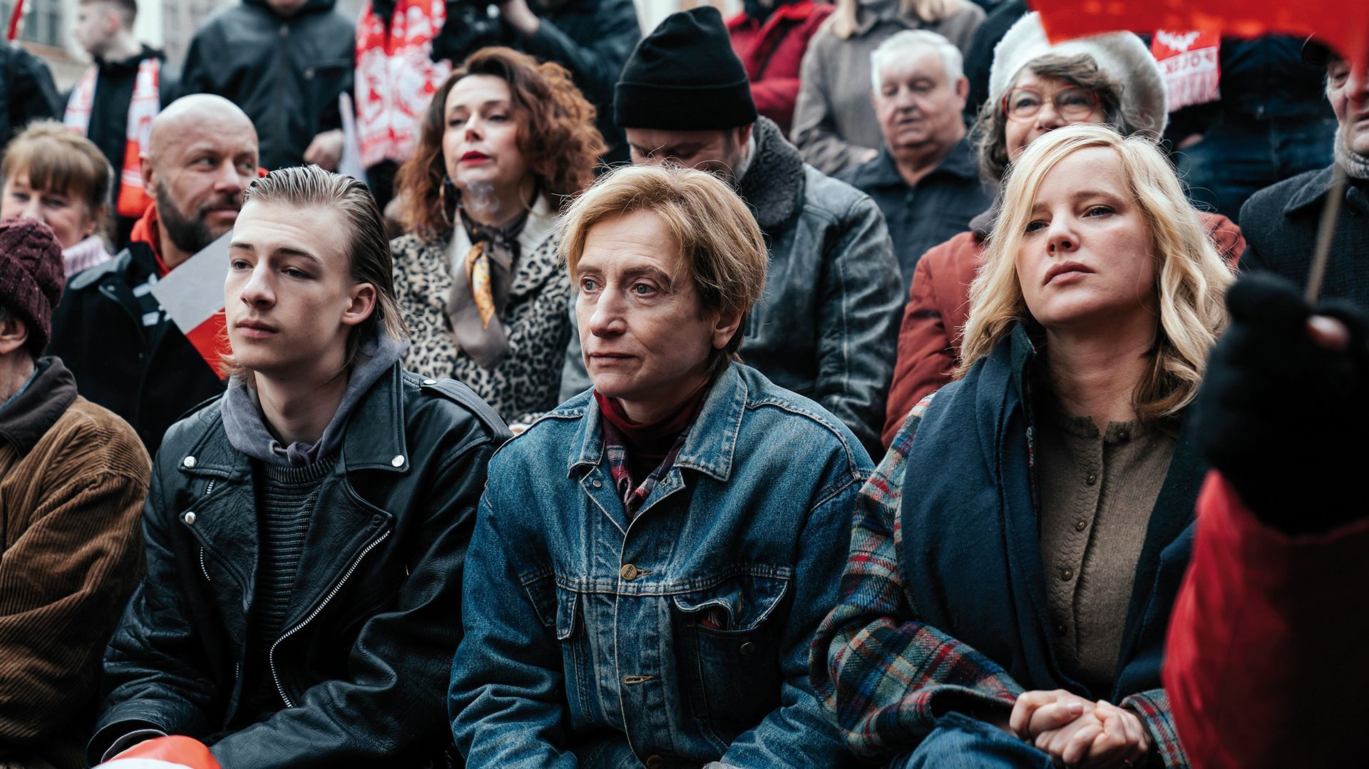 Eine Gruppe von Menschen sitzt bei einer Demonstration in einer Menschenmenge.