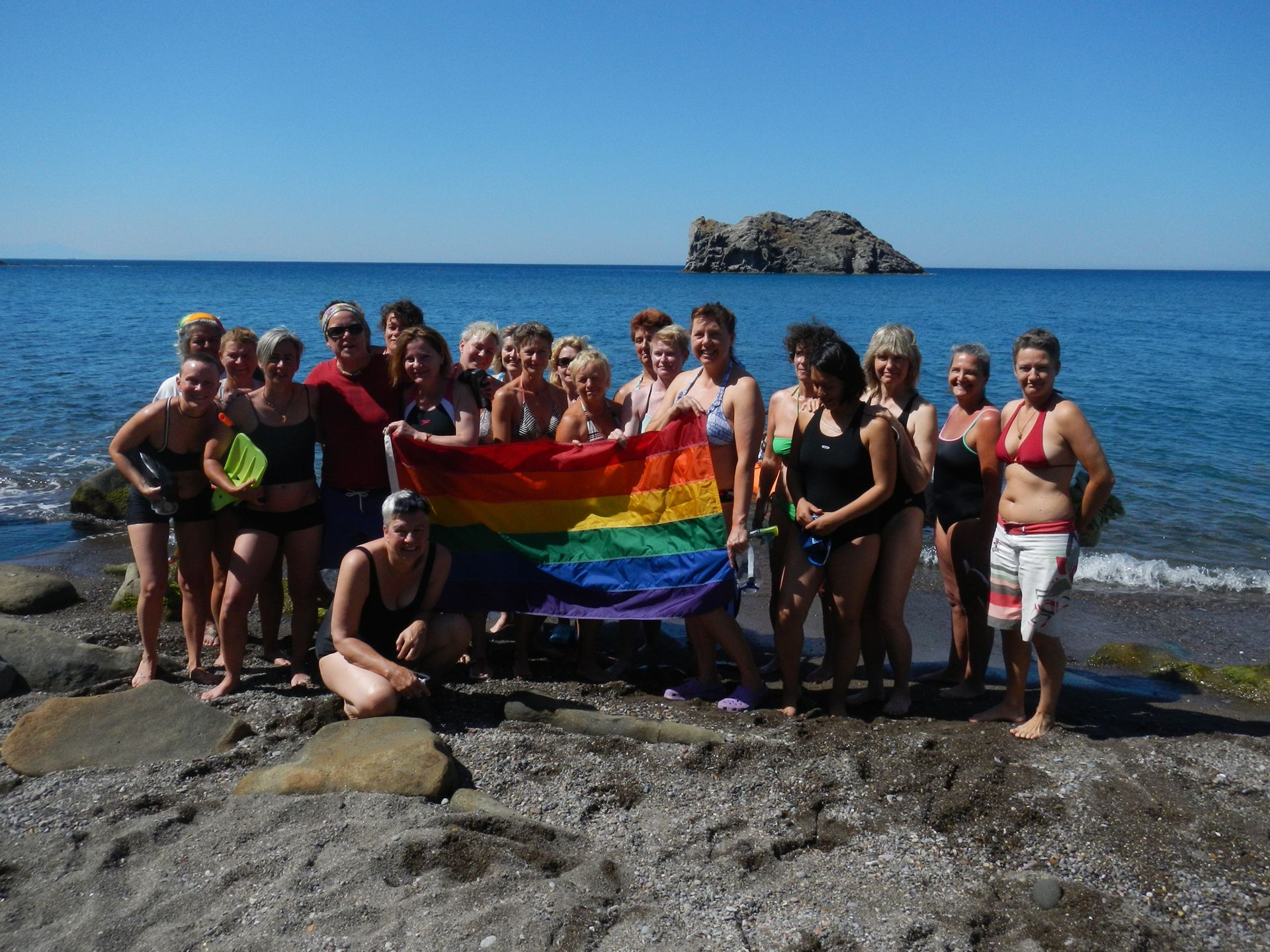 Eine Gruppe von Menschen hält eine Regenbogenfahne am Strand