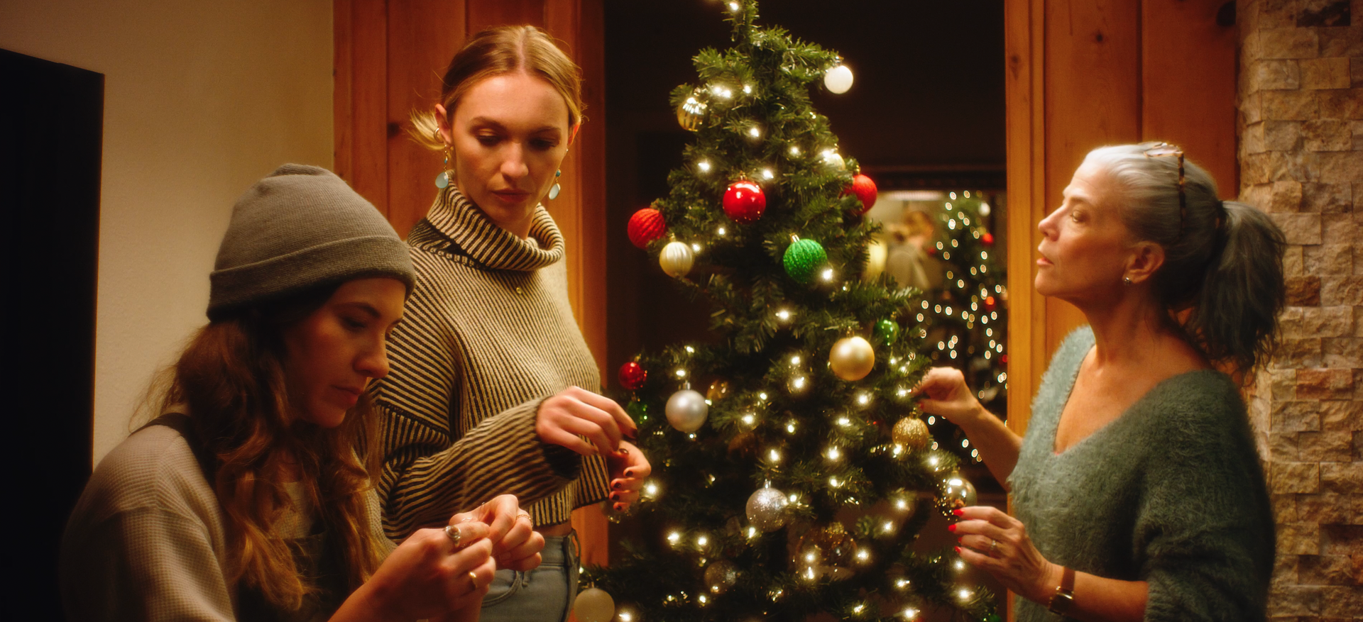 Drei Frauen schmücken in einem Wohnzimmer einen Weihnachtsbaum.