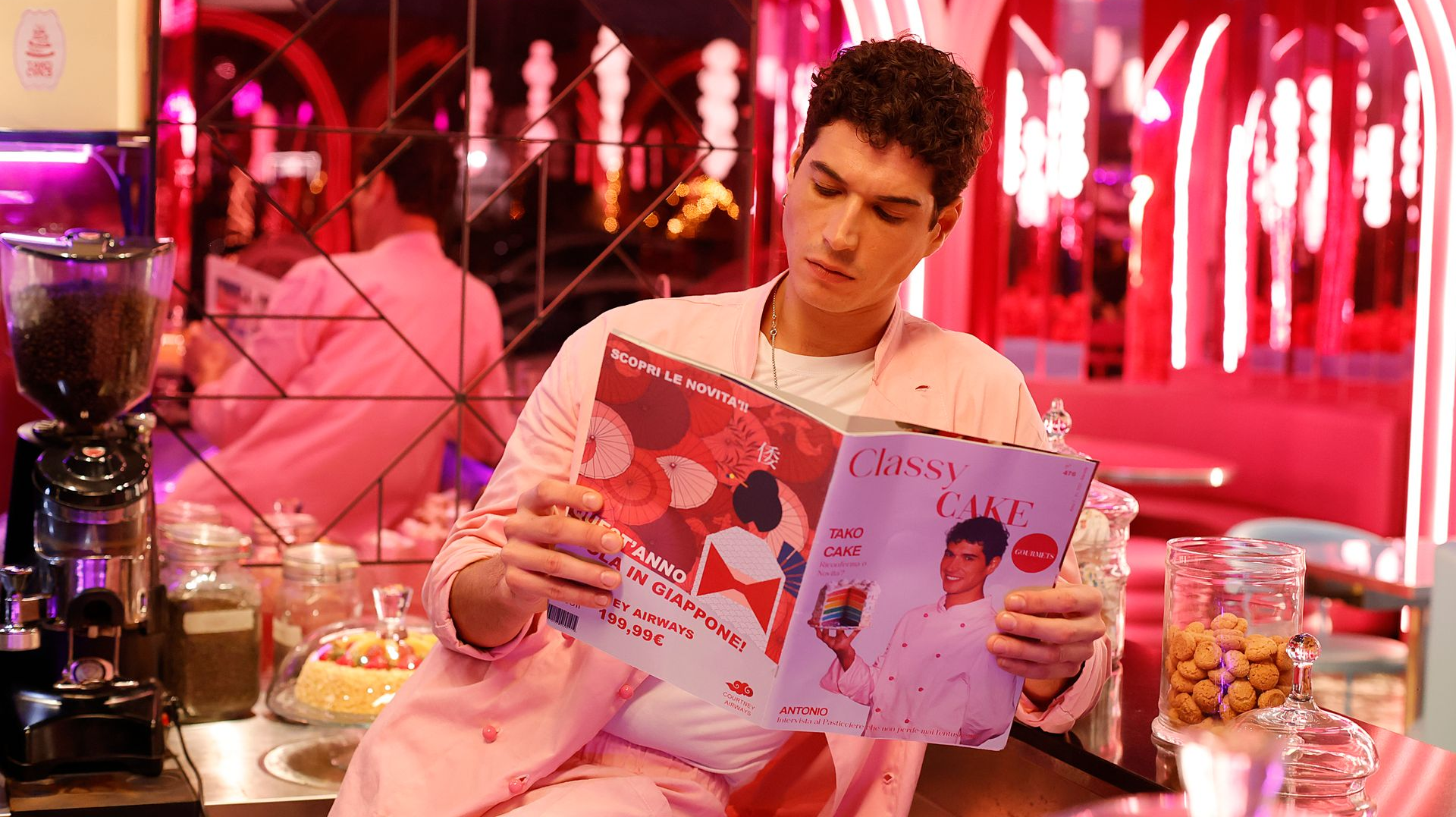 Mann im rosa Anzug liest Zeitschrift in einem rosa Diner, umgeben von Neonlichtern.