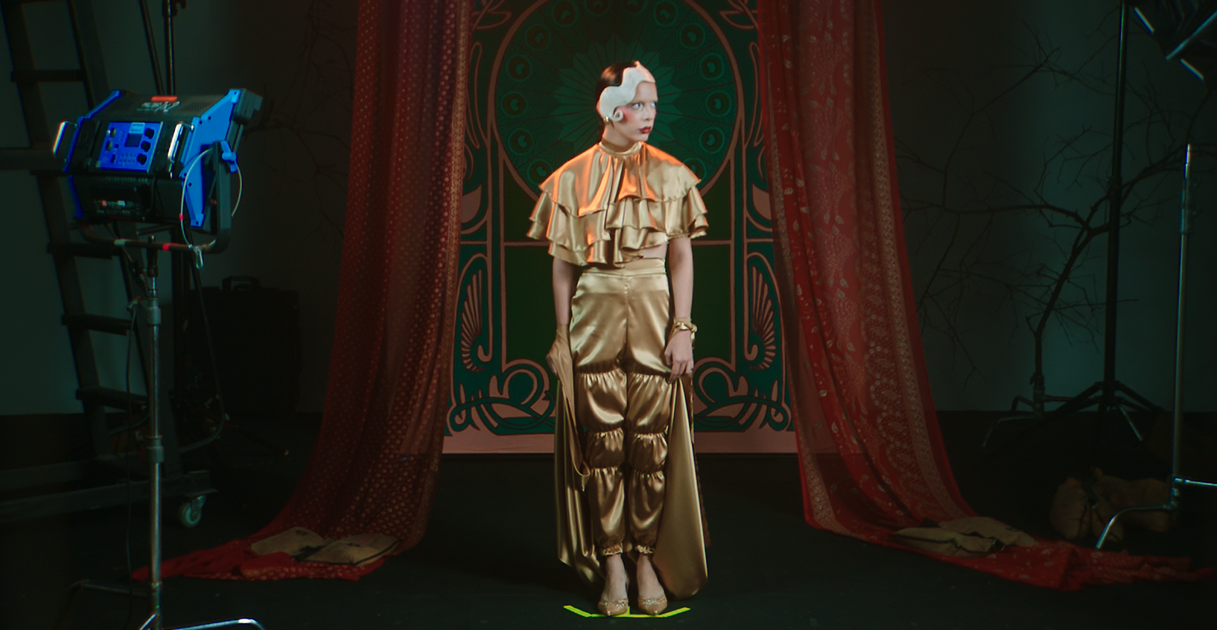 Eine Person in einem goldenen Kleid steht vor einem Hintergrund, der von Studiolichtern beleuchtet wird.