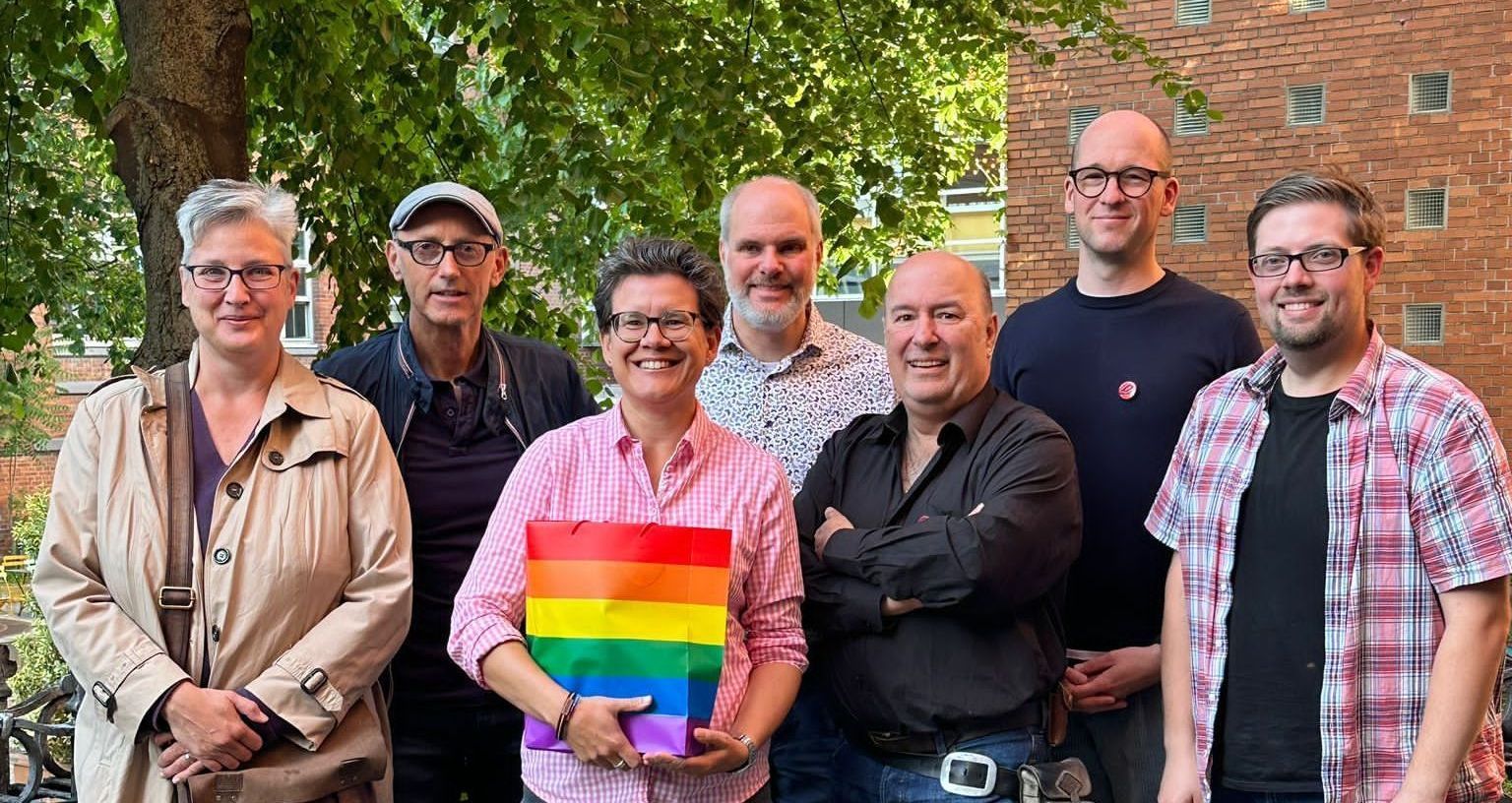 Eine Gruppe von Menschen, die nebeneinander stehen und eine Regenbogenfahne halten