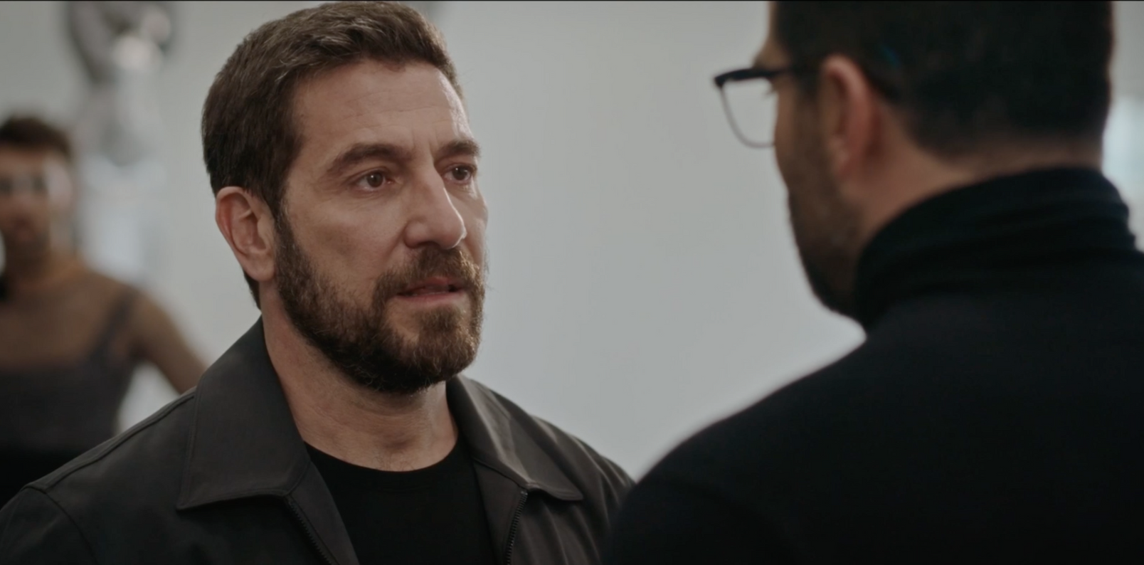 Zwei Männer unterhalten sich in einem Studio. Einer mit Bart und grauer Jacke, der andere mit Brille und schwarzem Rollkragenpullover.