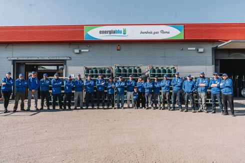 Gruppo di operai in uniforme blu in posa davanti a un edificio e a un veicolo di servizio di energyBIZ.
