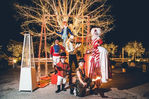 Persone in costume festivo posano all'aperto di notte, con alberi illuminati e un riscaldatore da patio acceso.