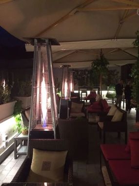 Salotto esterno coperto con divani e sedie rossi e un alto riscaldatore da patio per la notte