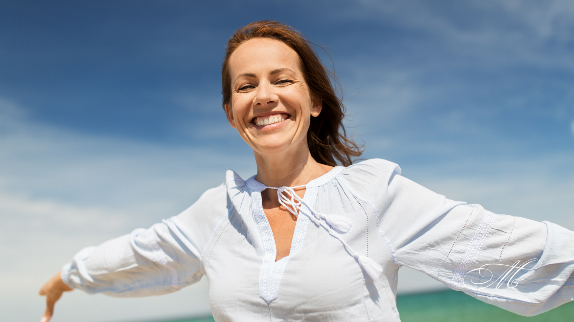 A woman is standing on the beach with her arms outstretched and smiling.