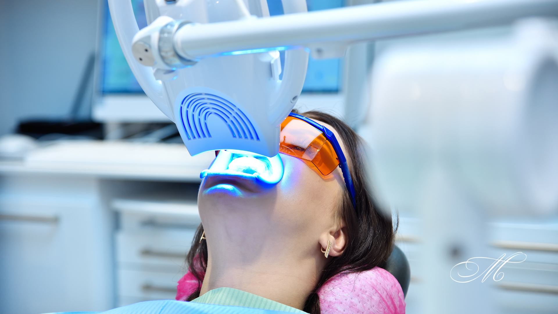 A woman is getting her teeth whitened in a dental office.