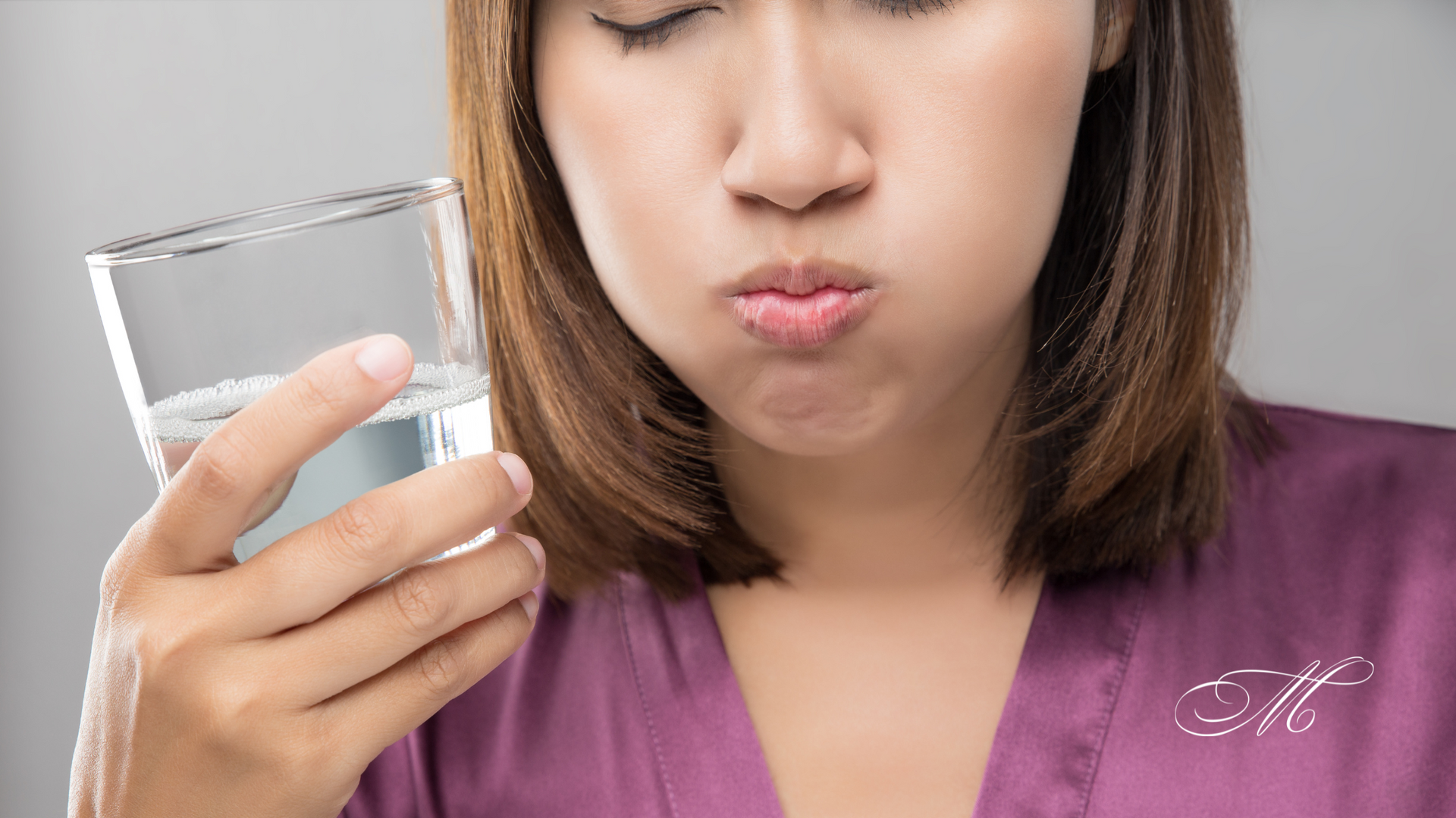A woman is holding a glass of water in her mouth.