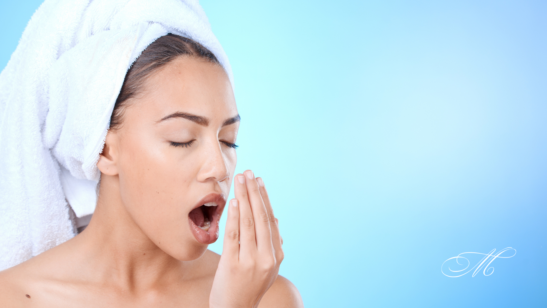 A woman with a towel wrapped around her head is covering her mouth with her hand.