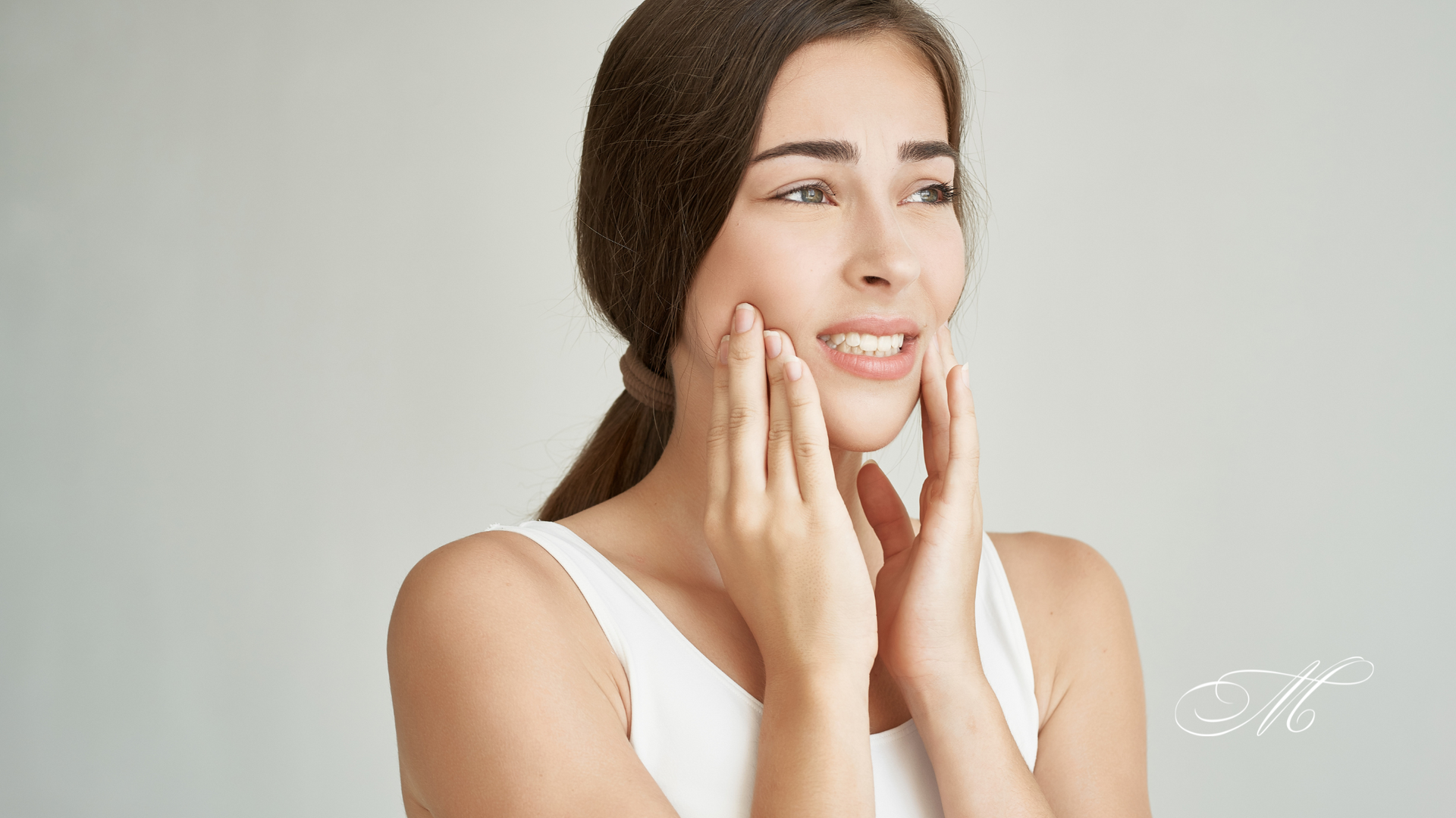 A woman is touching her face with her hands and smiling.