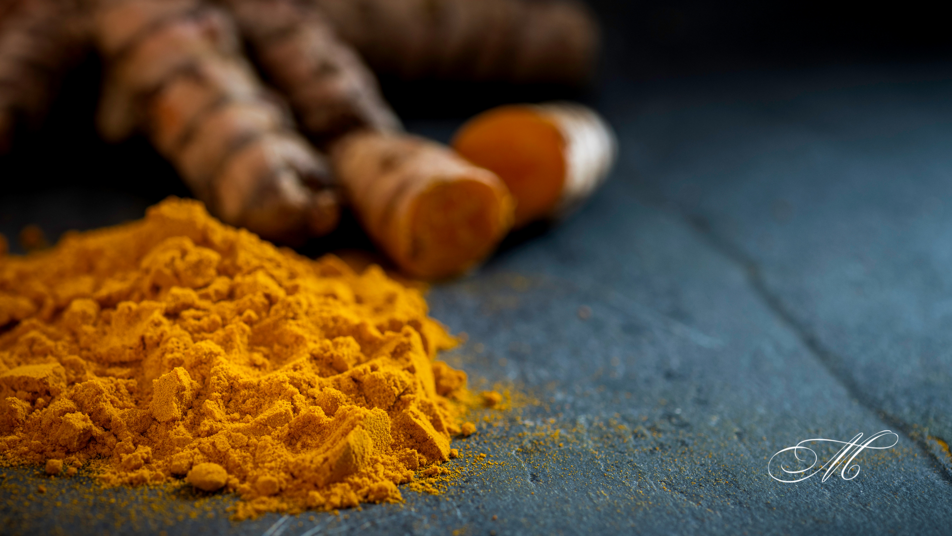 A pile of turmeric powder next to turmeric roots on a table.