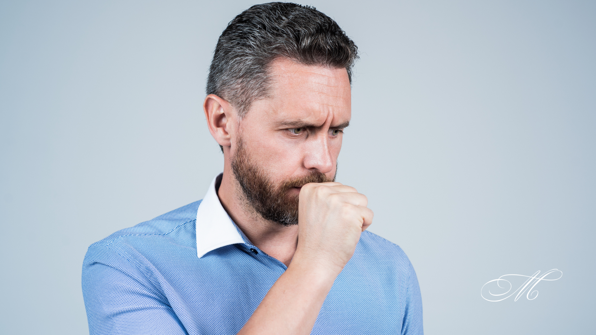 A man with a beard is coughing into his hand.