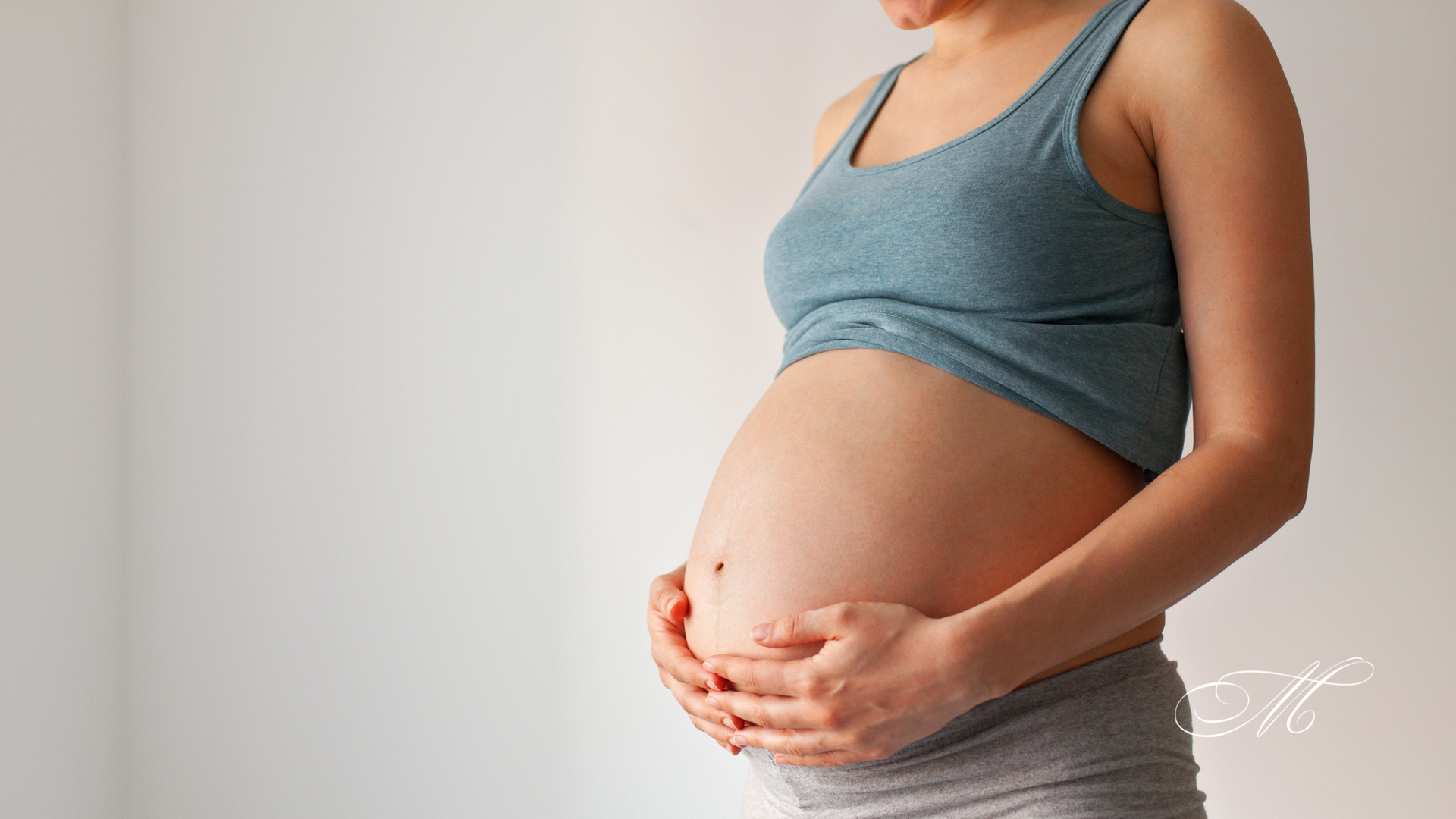 A pregnant woman is holding her belly with her hands.
