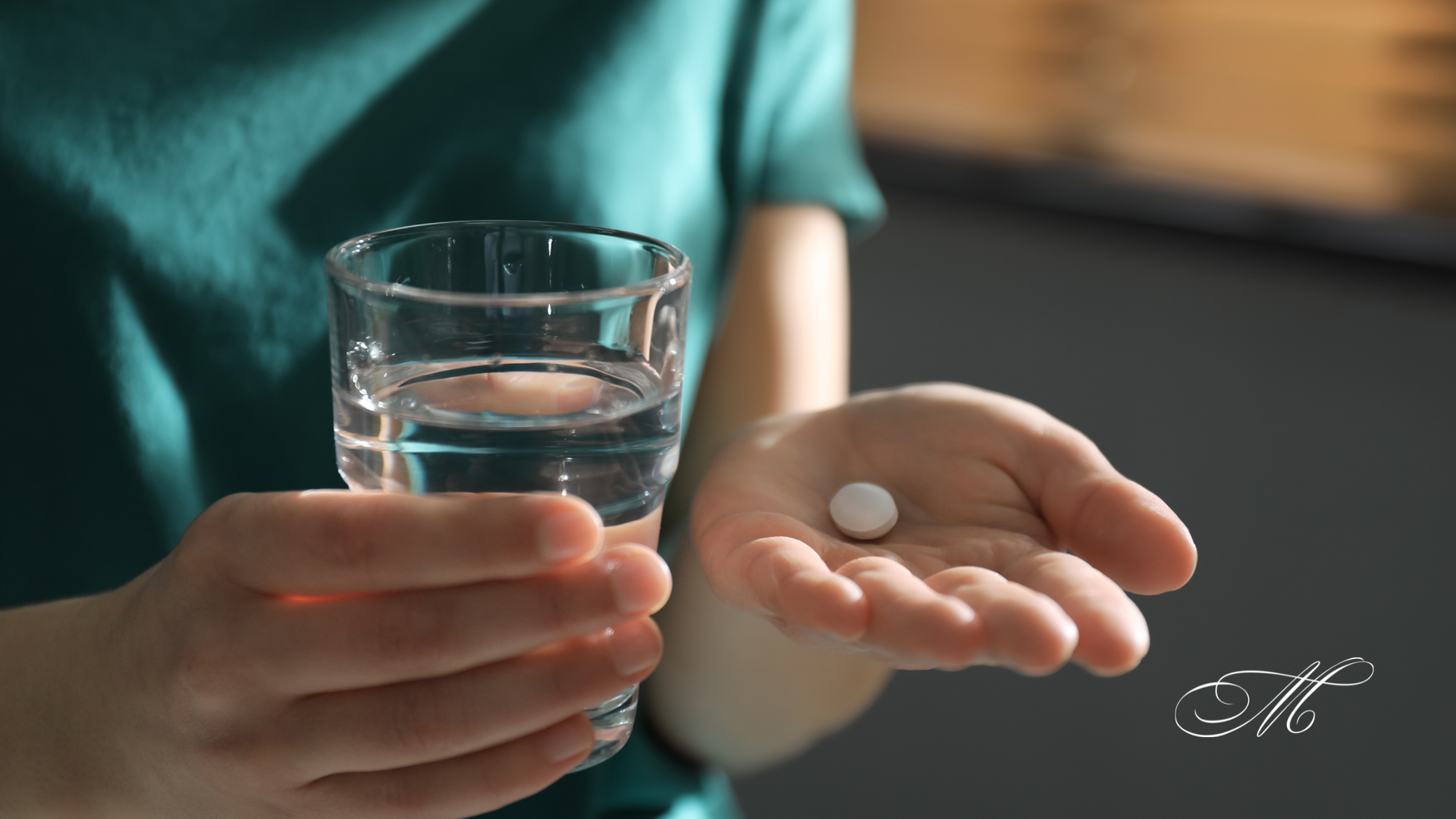 A person is holding a glass of water and a pill in their hand.