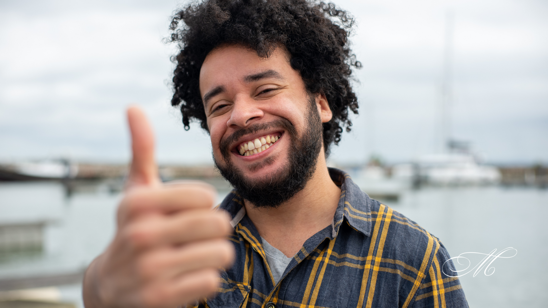 A man with curly hair and a beard is smiling and giving a thumbs up.