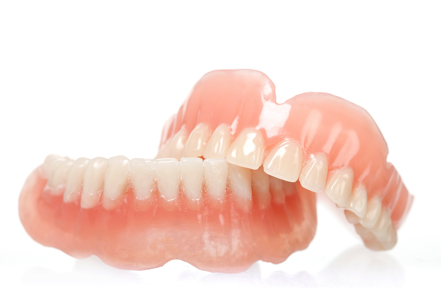A pair of full upper and lower dentures with pink acrylic gums and white teeth set against a white background.