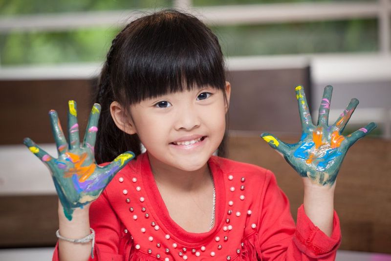 A little girl with her hands painted in different colors - Lala's Lullaby's Group Family Daycare