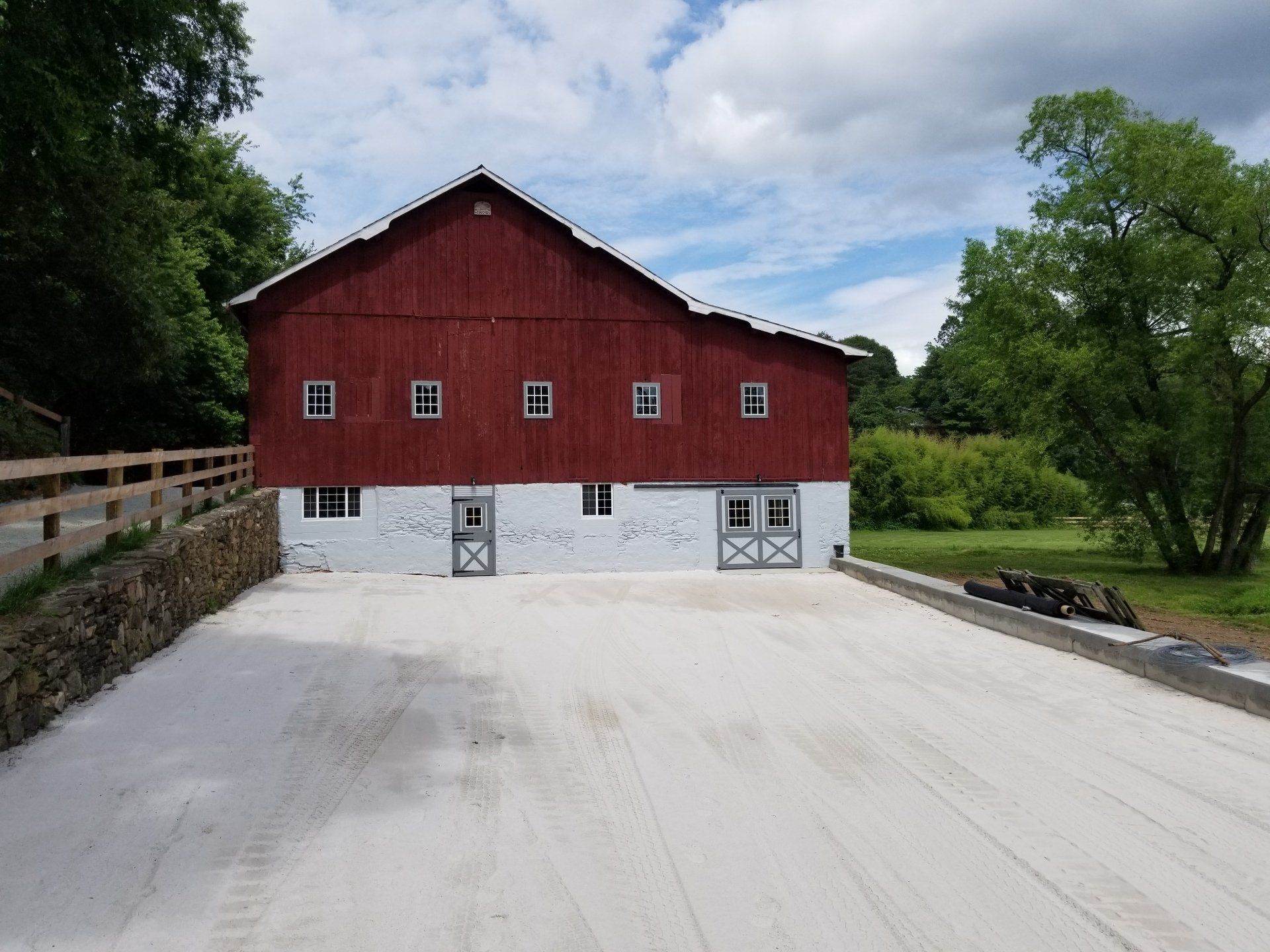 Red and white barn with a gravel driveway on a sunny day.