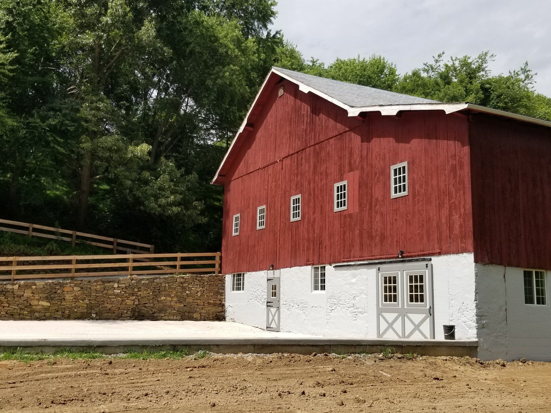 Red barn with white lower section; windows and double doors. Trees and a fence in background.