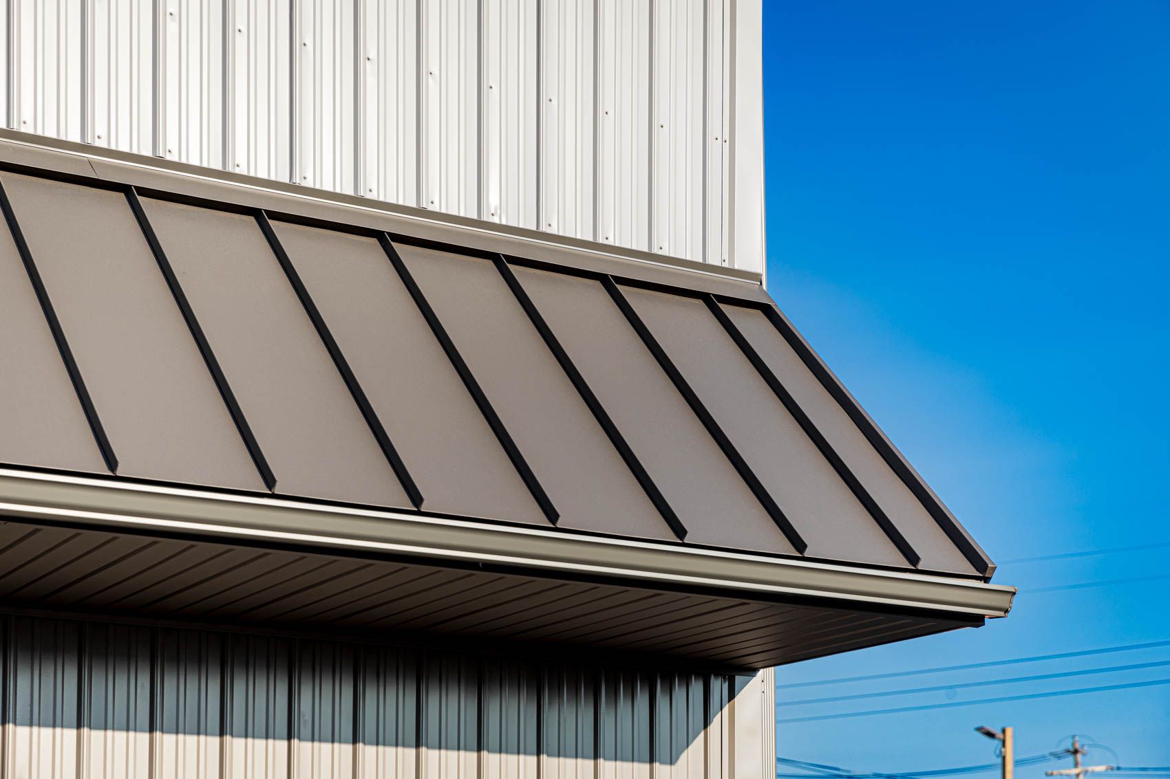 Grey metal awning on a white building against a blue sky.