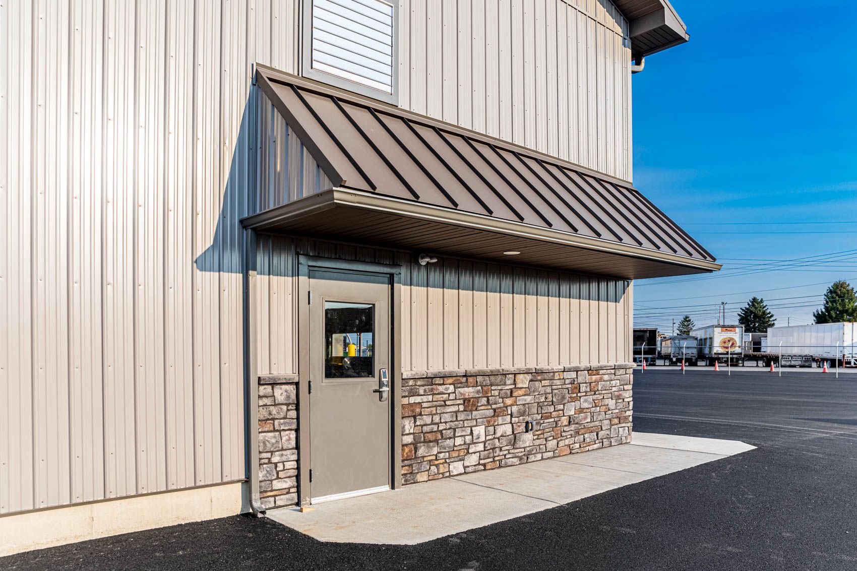 Exterior of a building with a metal awning over a door, stone veneer at the base, and a clear blue sky.
