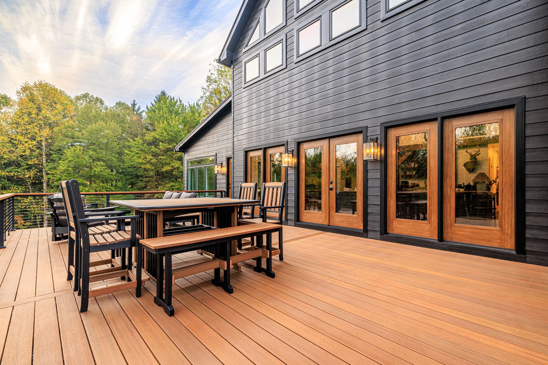 Wooden deck with outdoor dining set in front of a modern, dark-sided house with glass doors.