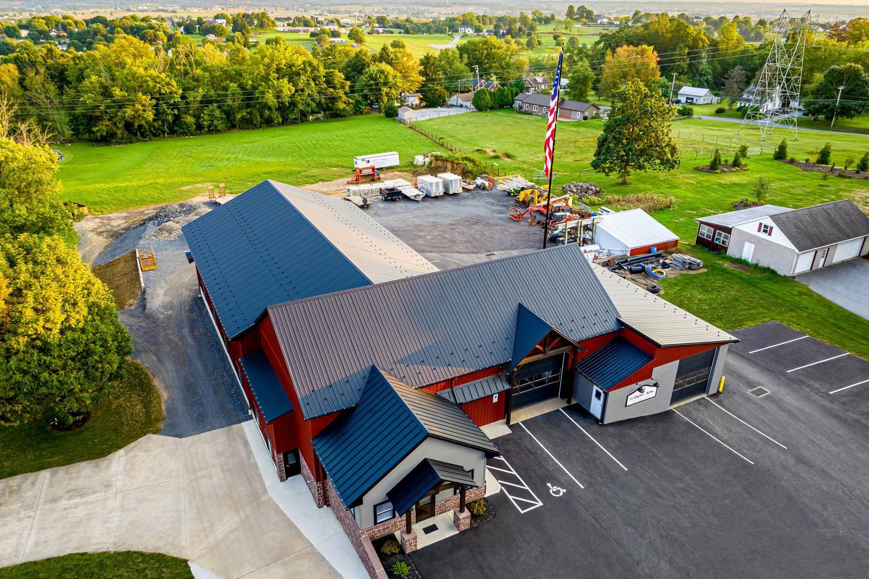 Aerial view of a red building with a dark blue roof, parking lot, and rural landscape in the background.