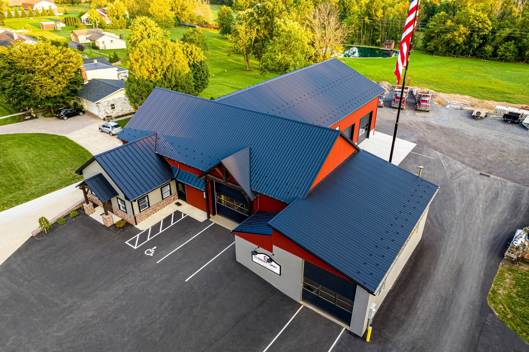 Aerial view of a fire station with a dark blue roof, parking lot, and an American flag.