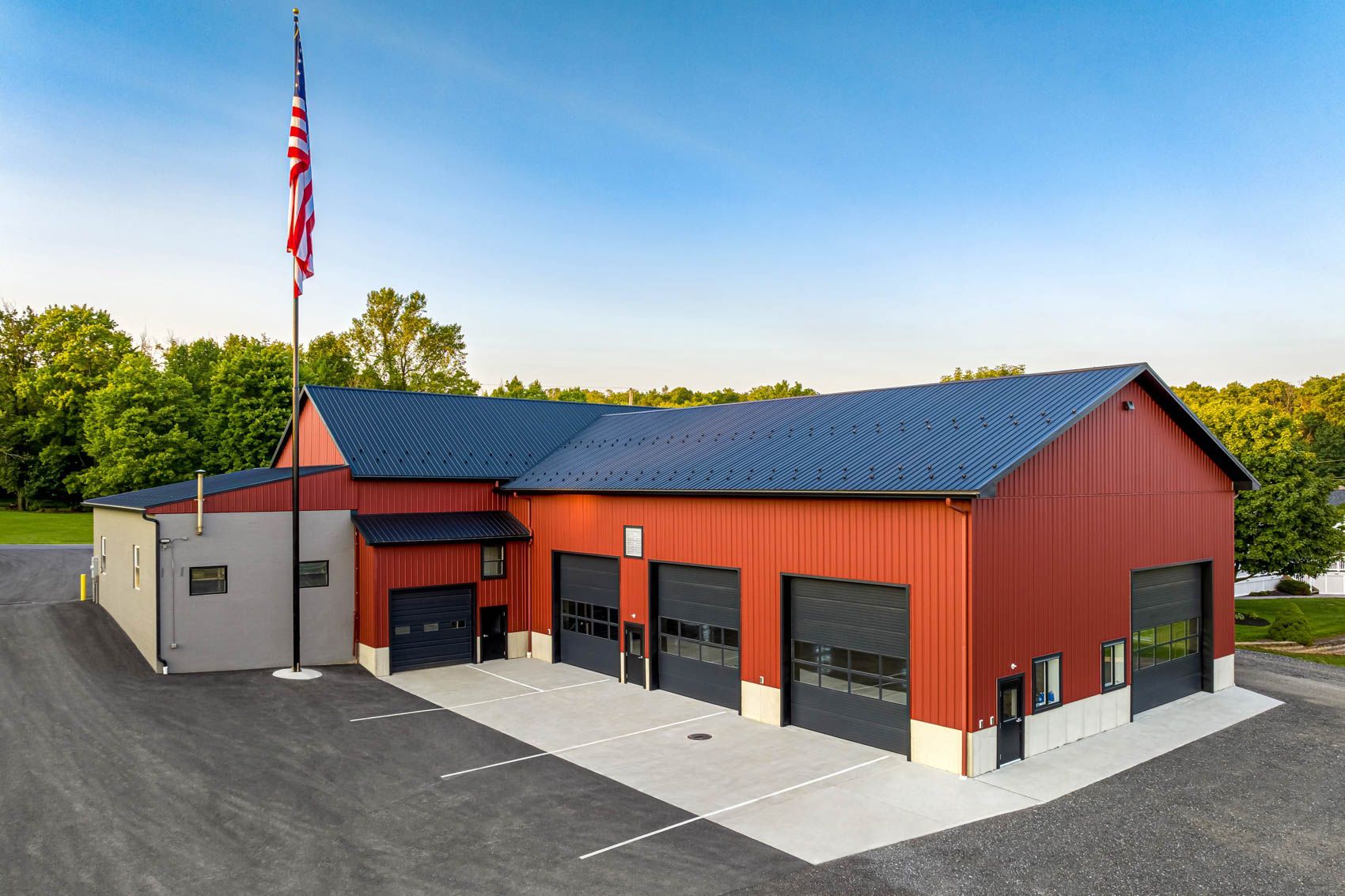 Red fire station with black garage doors, blue roof, and American flag on a sunny day.