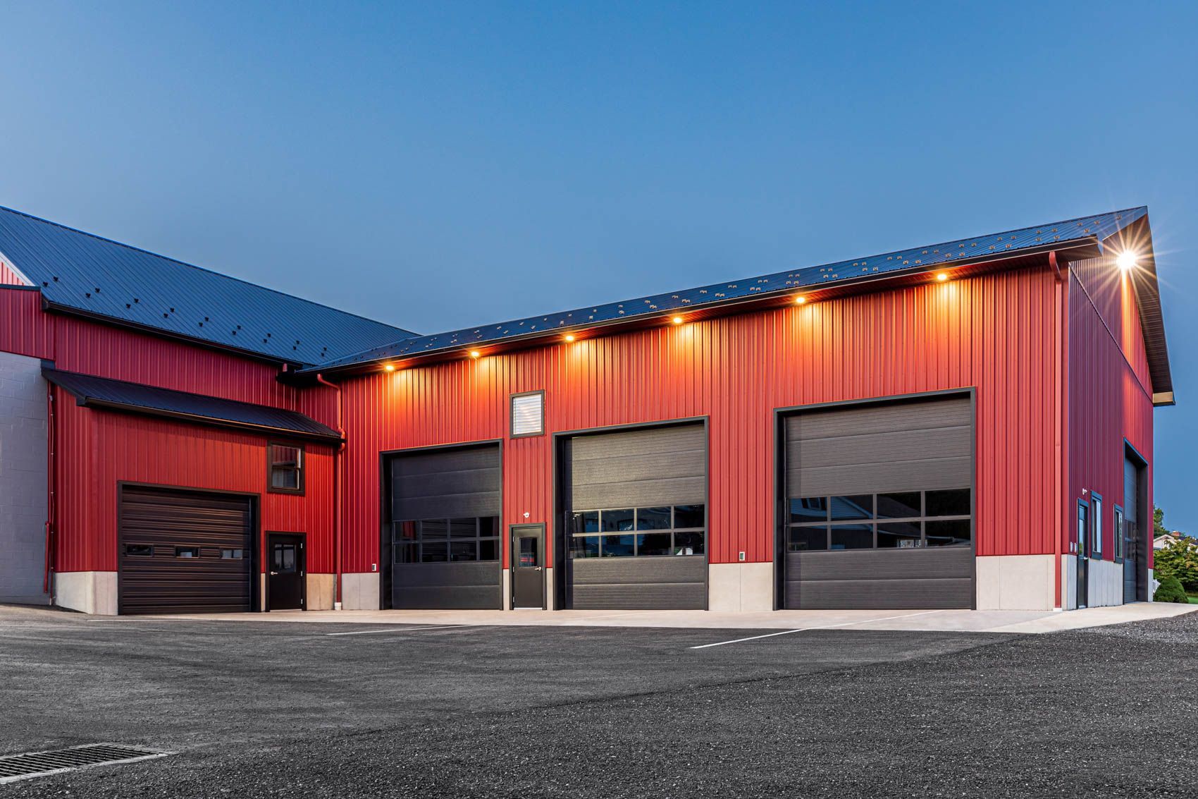 Red metal building with black garage doors, under a dark blue sky.