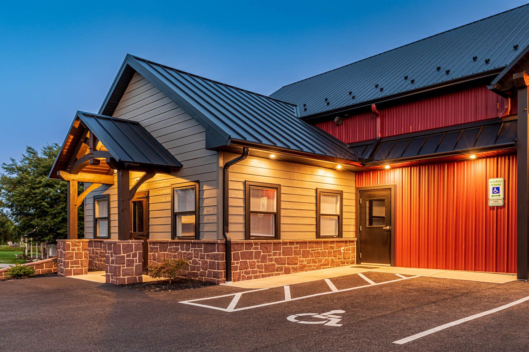 Exterior of building with red and tan siding, a dark roof, and a handicap parking space.