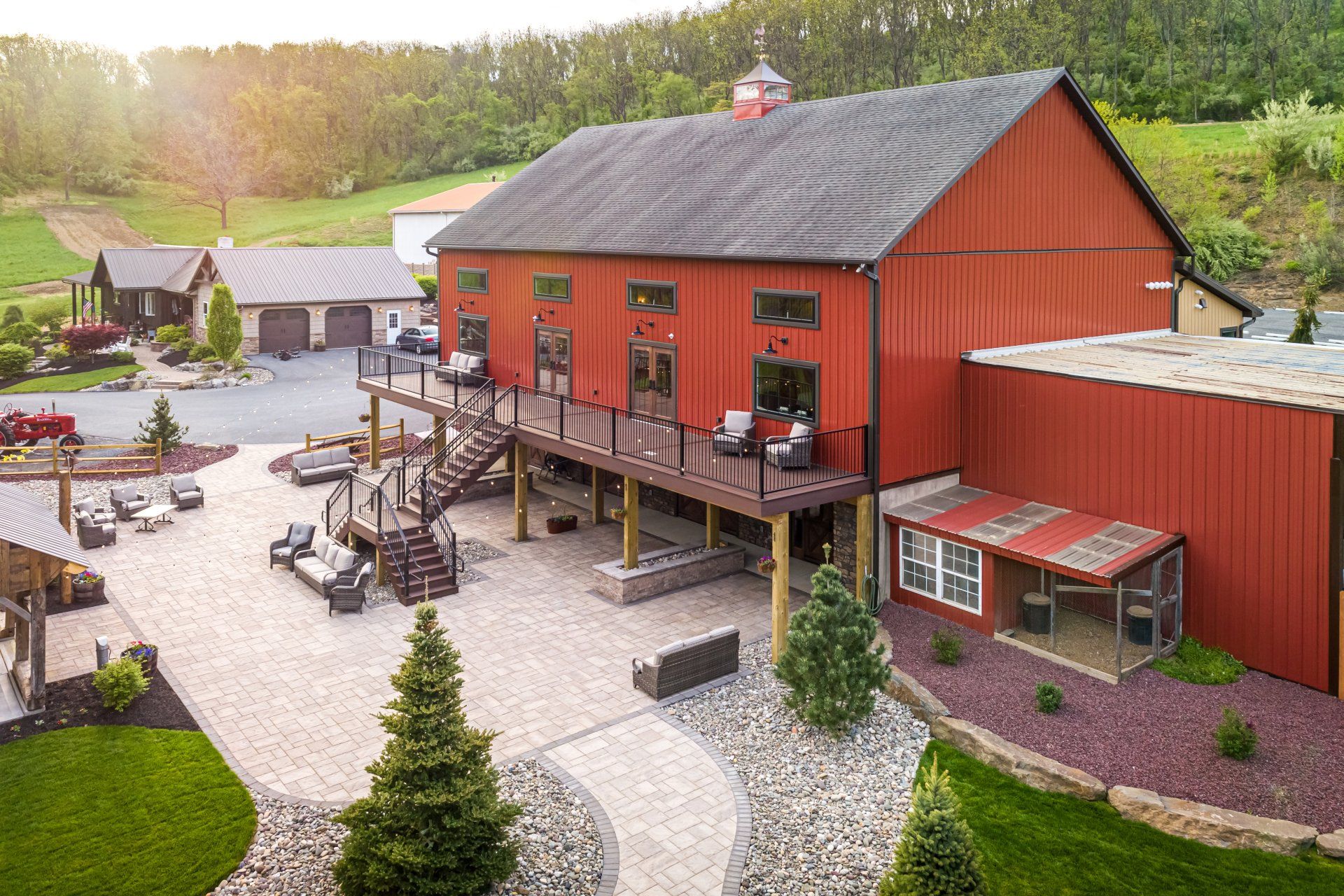 Red barn with deck, patio seating, and small building. Trees and green landscape surround.