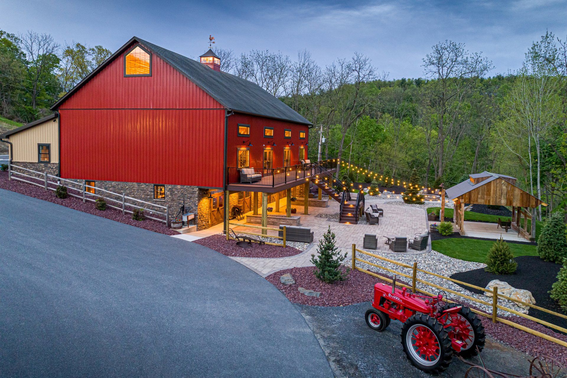 Red barn with outdoor patio and tractor, dusk setting.